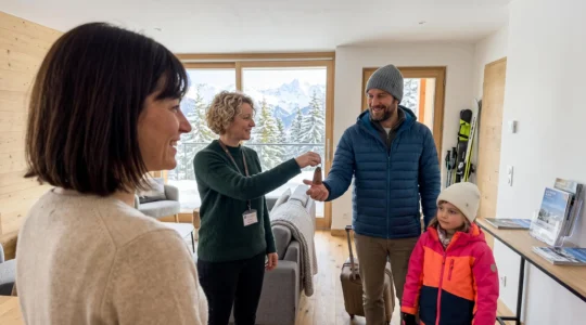 Une famille de quatre personnes vue de dos reçoit les clés d'un appartement de station par un agent immobilier local dans un intérieur alpin contemporain lumineux