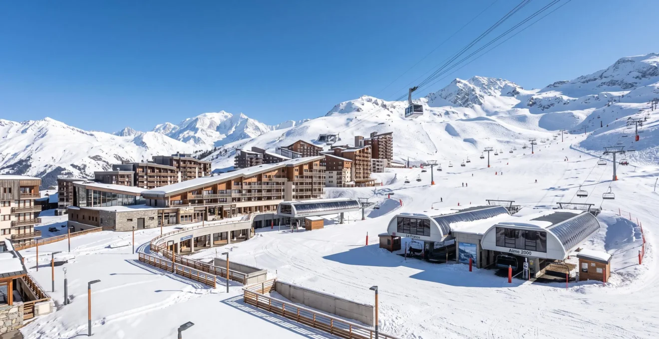 Vue panoramique de la station de La Plagne en hiver, avec ses bâtiments modernes d'altitude et les pistes de ski enneigées sous un ciel bleu éclatant